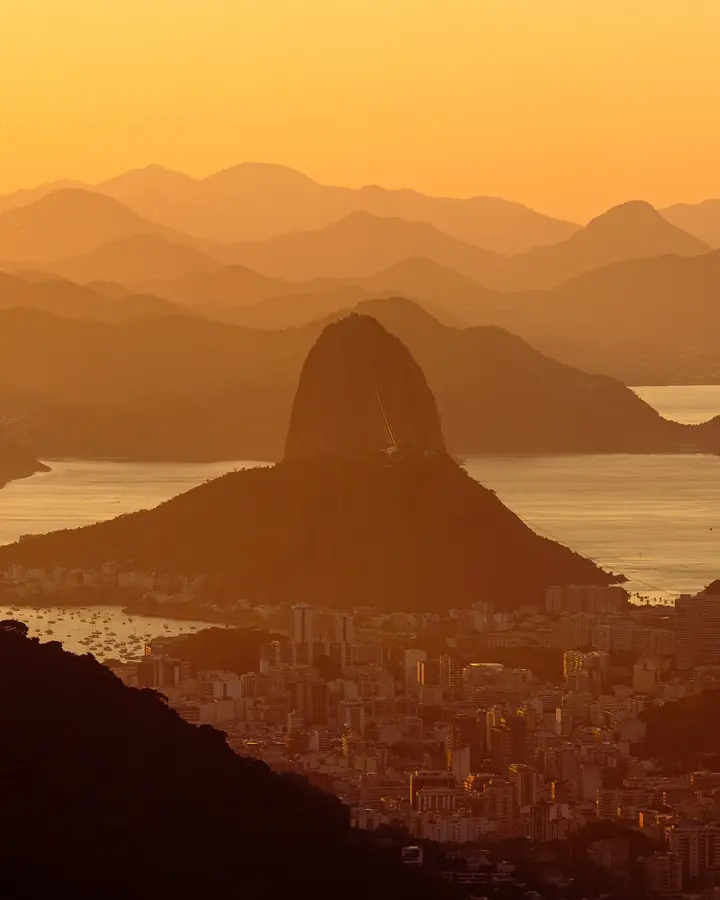 O Pão de Açúcar e as serras da Baía de Guanabara ao amanhecer, em tons de dourado.